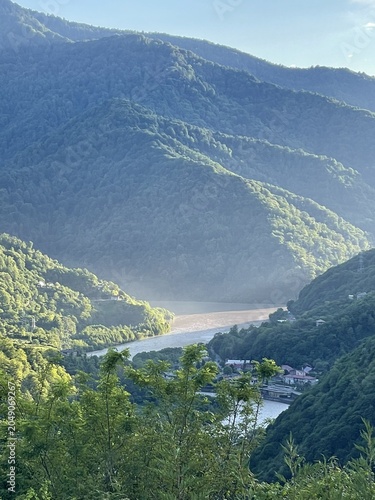 A serene landscape featuring lush green mountains surrounding a winding river. The scene captures the tranquility of nature in a remote area.
