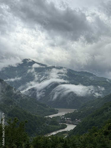 A scenic view of mountains under a cloudy sky. The landscape features lush green hills and a winding river flowing through the valley.