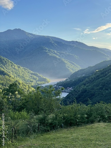 A scenic view of a lush green valley surrounded by mountains. The river flows through the valley, with mist rising in the early morning light.