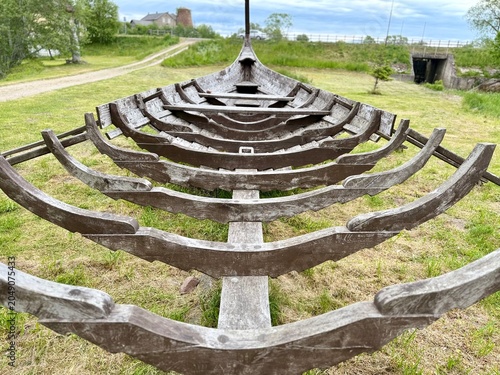 A front view showing the structural wooden ribs and skeleton framework of a historic Viking ship replica on display in a park in Latvia.