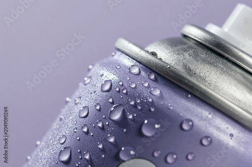 Spray can features lavender coating covered in translucent water droplets. Metal rim rests near a white nozzle against a soft purple backdrop with bright specular highlights.