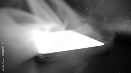 Black and white smartphone illuminating with smoke and particles in a dark environment