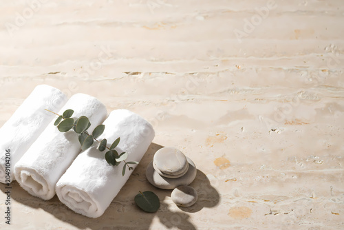 Rolled white towels with green eucalyptus leaves and stones on marble surface transparent background