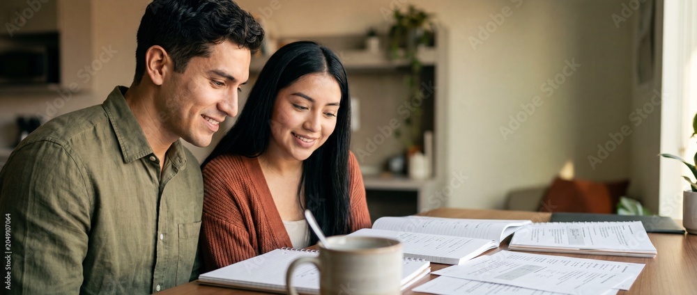 Fototapeta premium Hispanic couple studying at home together, reviewing financial documents and notebooks at desk, smiling partners planning future budget, remote work, adult education, distance learning happy lifestyle