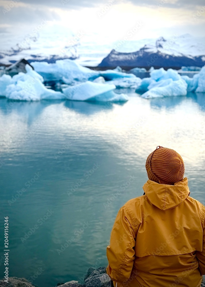 Fototapeta premium A hiker in yellow looks out over Jökulsárlón, Iceland's largest glacier lagoon, located in southeastern Iceland.