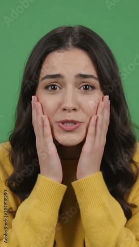Young woman looking at camera with shocked and surprised face expression on green screen.