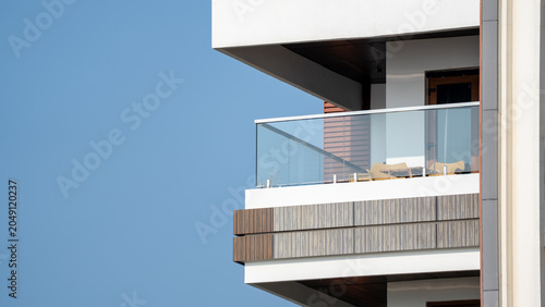 Modern apartment building corner balcony with glass railing and wood cladding against blue sky