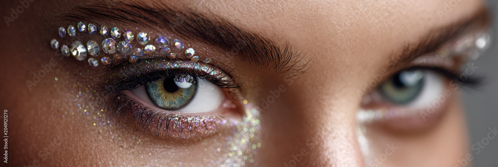 Naklejka premium Woman's eyes highlighting creative makeup application with colorful glittering rhinestones and shimmery glitter, creating a captivating party and glamour beauty look