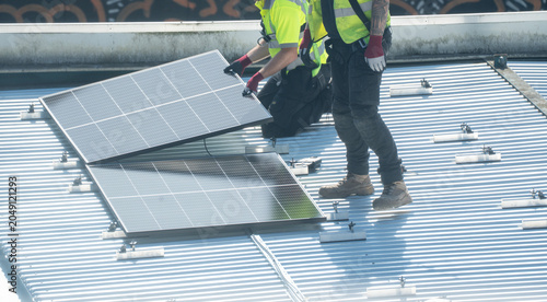 Two worker in yellow vest installing solar panel on metal rooftop surface