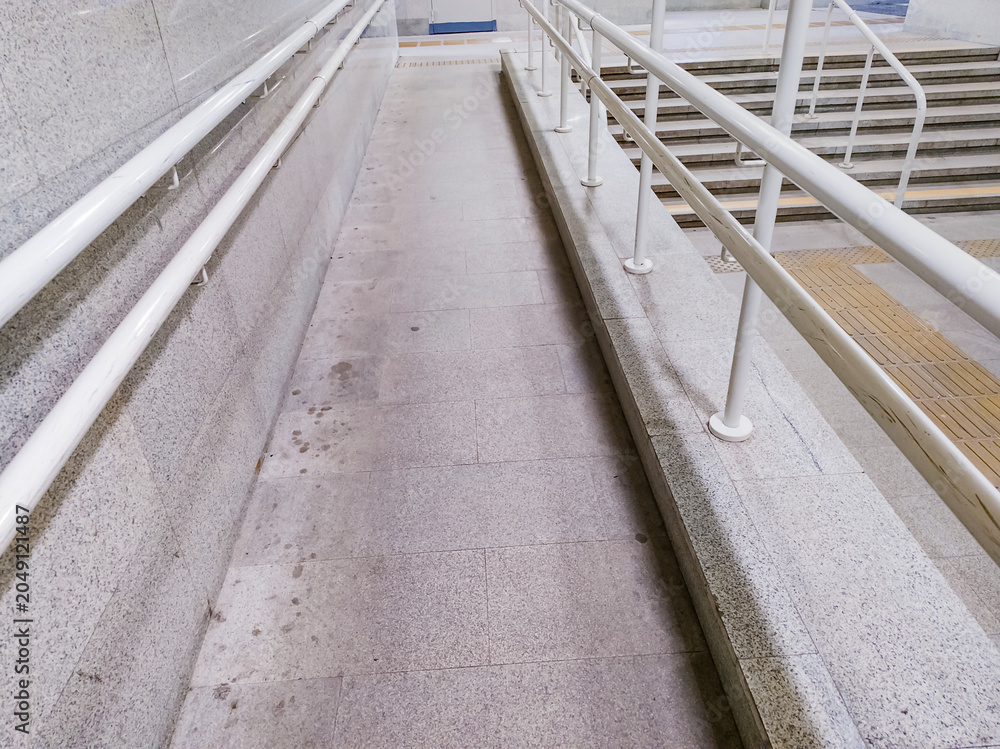 Obraz premium Stone accessibility ramp with white metal handrails next to stairs. Public facility infrastructure with yellow tactile paving