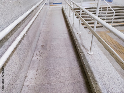 Stone accessibility ramp with white metal handrails next to stairs. Public facility infrastructure with yellow tactile paving