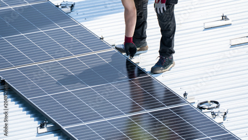 Worker standing beside installed solar panel row on flat metal rooftop surface