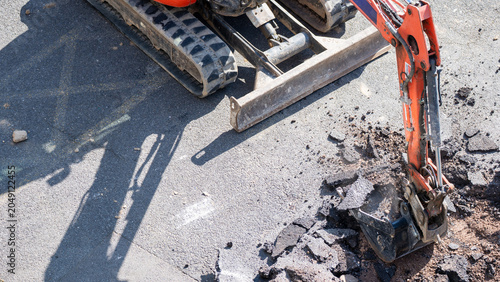 Foto Mini excavator digging into broken asphalt pavement with bucket on road surface