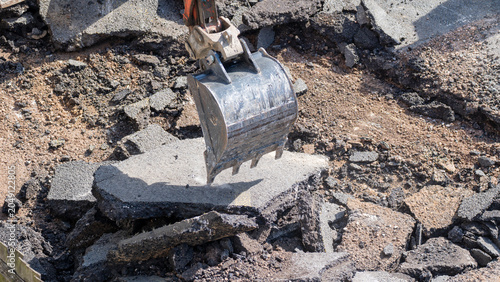 Foto Excavator bucket crushing broken asphalt slab with gravel and rubble underneath