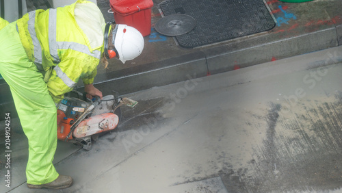 Construction worker in yellow vest cutting concrete pavement with circular saw on road