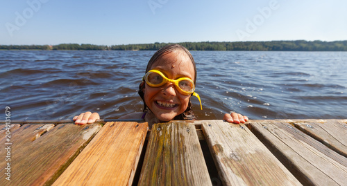 Bild auf Leinwand Child wearing goggles looks into lake water from wooden dock discovering underwater world with wonder