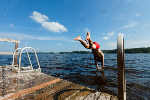 Фотография Man dives off pier with arms spread entering lake water on sunny summer day