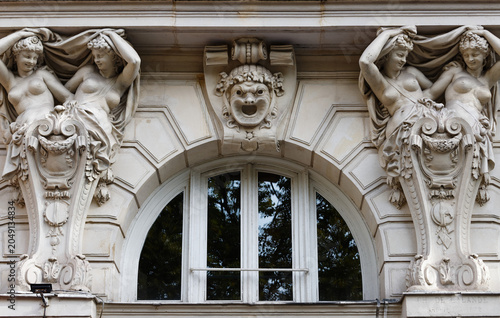 Stunning architectural detail of a classical Parisian building facade featuring two elegant female atlantes in draped robes raising their arms to support an entablature, flanking an arched window.