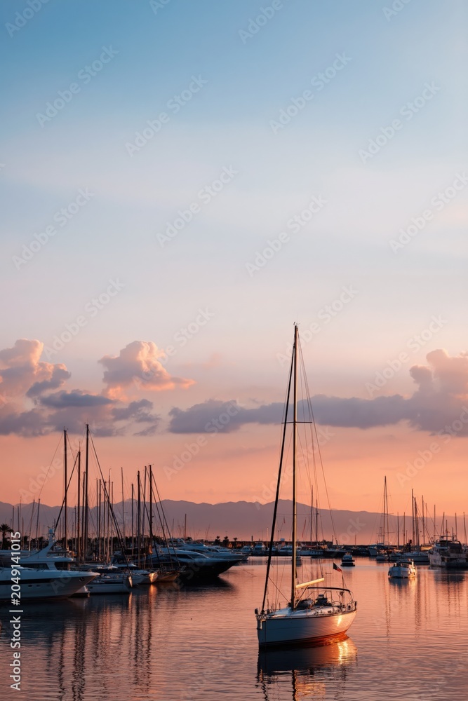 Obraz premium Single sailboat reflecting on harbor water during pink sunset