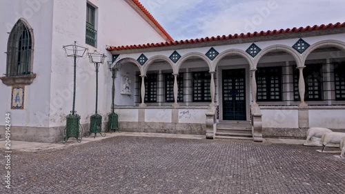 Traditional Portuguese church architecture featuring a stone paved courtyard under bright daylight with arched arcades decorative iron street lamps and white walls