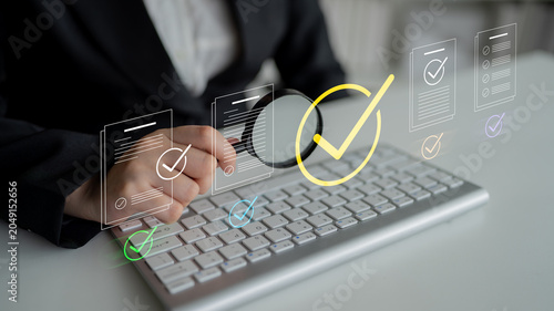 Photos A business professional sitting at a desk reviews important documents using a keyboard while digital checklist graphics illustrate the process of compliance and quality assurance