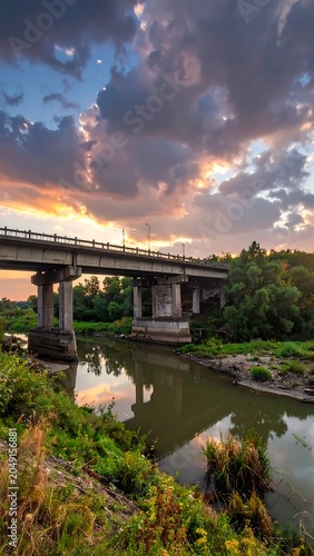 Serene riverside sunset with wooden bridge and lush greenery.