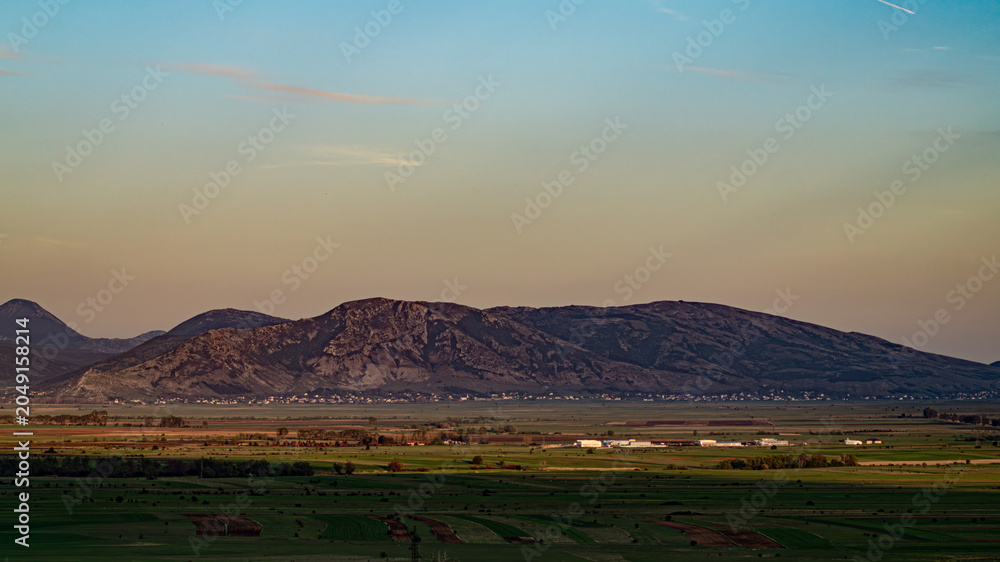 Fototapeta premium Wide landscape view of an agricultural valley plain against a massive karst mountain range at sunset.