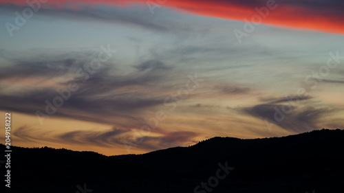 Beautiful sunset sky gradient with wispy clouds over dark mountain silhouettes and a fiery red cloud streak.