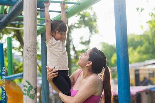 Photography Proud Latina mother smiling as she helps her daughter come down from the monkey