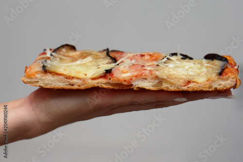 Foto Side profile view of a thick, porous rectangular slice of pizza parmigiana held