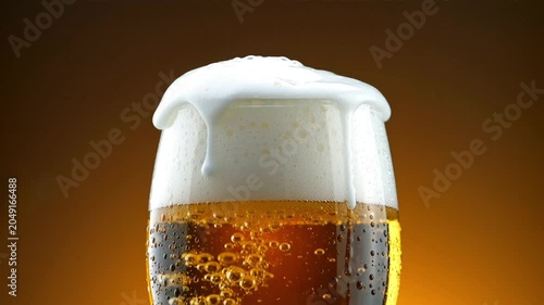 Glass of fresh light beer with white spilling foam bubbles and drops