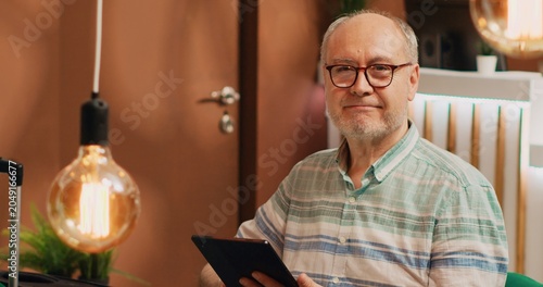 Canvas Print Older man tourist on lounge area sofa, surfing the web on digital tablet