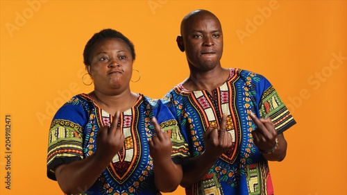 Photos Rude ethnic couple showing middle finger in studio, doing offensive provocative gesture over orange background