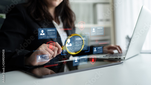 Foto Business Professional Analyzing Digital Data with a Magnifying Glass on a Tablet Displaying User Profiles and Security Icons in an Office Setting