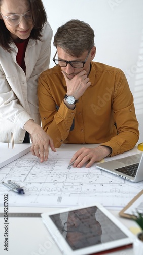 Architecture professionals collaborating on a housing project  studying detailed blueprints and a scaled 3d model  discussing design ideas for urban planning and modern construction