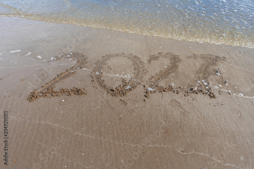 A wave was washing away the “2027” written in the sand on the beach.
