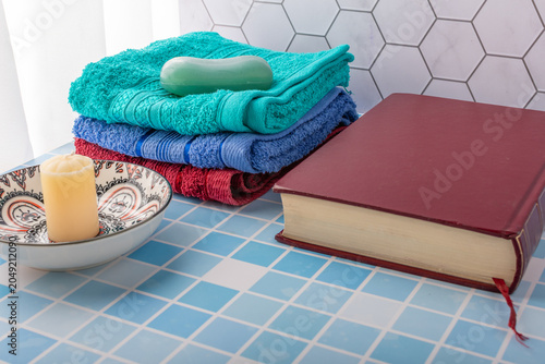 A stack of colorful towels, a bar of soap, a book, and a candle.