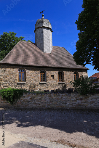 Historische Dorfkirche mit markantem Turm hinter einer Mauer im Sonnenschein, Meuschau, Merseburg, Saalekreis, Sachsen-Anhalt, Deutschland