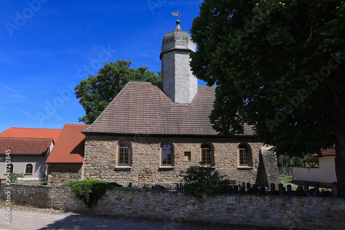 Seitenansicht der historischen Dorfkirche aus Feldsteinen hinter einer Steinmauer im Sommer, Meuschau, Merseburg, Saalekreis, Sachsen-Anhalt, Deutschland