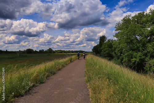 Radfahrer auf dem Elster-Radweg durch eine idyllische Wiesenlandschaft unter einem spektakulären Wolkenhimmel, Ermlitz, Schkopau, Saalekreis, Sachsen-Anhalt, Deutschland