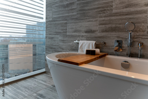 Modern luxury bathtub featuring a rustic wooden tray with spa amenities and towels
