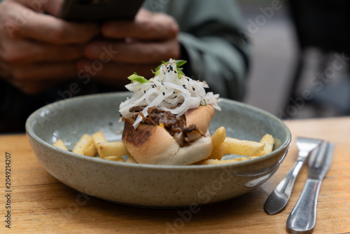 Modern cafe lunch meal featuring a gourmet meat roll and golden french fries in a ceramic dish