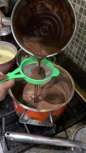 Hand Straining Ground Chocolate Into Boiling Pot on Kitchen Stove