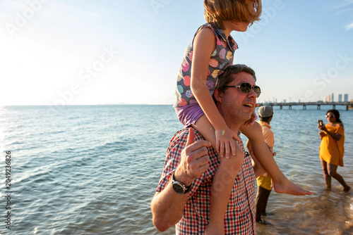 Photography Man carrying child on shoulders at the beach, sunny day scene.