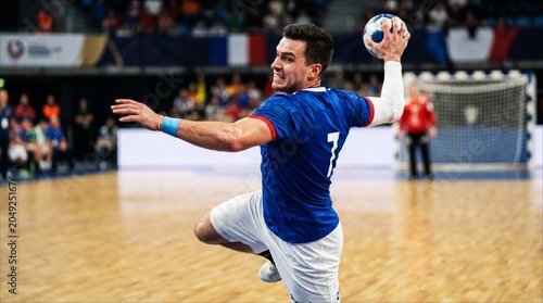 Handball player in blue jersey jumping for a shot. Professional handball athlete jumping to score a goal in indoor arena