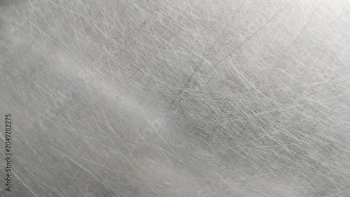 close-up of a scratched metal surface, possibly stainless steel or aluminum. The texture is rough, with numerous fine and deep scratches crisscrossing in various directions, creating a worn and aged