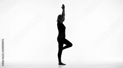 Silhouette of a senior woman practicing tree yoga pose with silhouette, wellness
