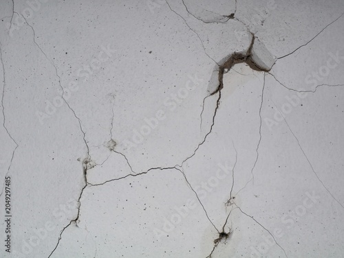 Texture of an old white concrete or stucco wall with severe cracks, deep fissures, and peeling plaster, representing construction damage, weathering, or structural failure