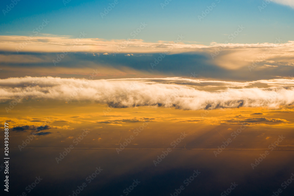 Fototapeta premium Bright evening sun rays pierce long fluffy cumulus cloud formations over the dark earth ground surface before the sunset time.