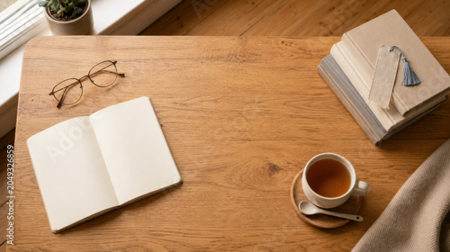 Cozy workspace wooden desk notebook tea cup book eyeglasses Warm morning light wooden desk with notebook, tea cup, book stack, eyeglasses